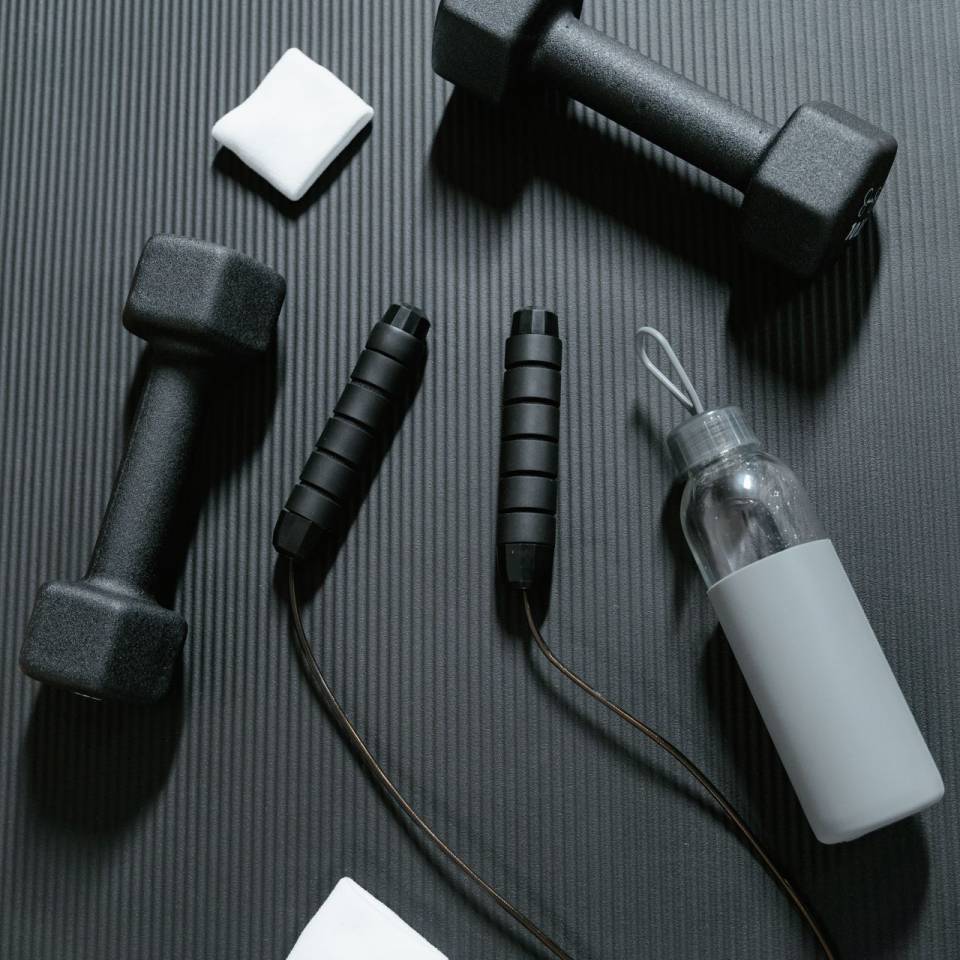 Hanteln und Flasche liegen auf einer Fitnessmatte